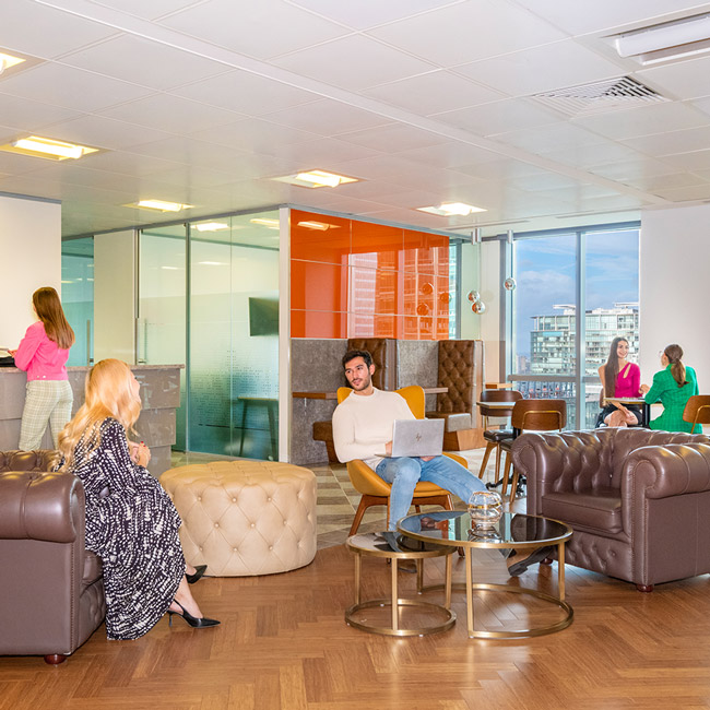 Clients working and networking at Canary Wharf coworking space with vibrant reception, and collaborative booths.